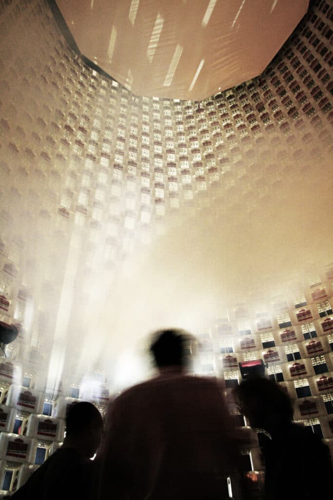 Szenografie, Umnutzung und Upcycling von KGRUPPE Architekten Basel - Ein Hochhaus-Interieur mit hunderten von Fenstern, beleuchtet mit diffusem Licht und nebulösen Silhouetten von Personen im Vordergrund.