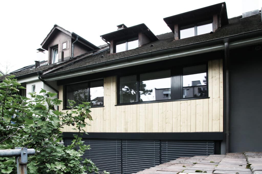 von KGRUPPE Architekten Basel - Mehrfamilienhaus mit Holzverkleidung und Dachbodenfenstern.