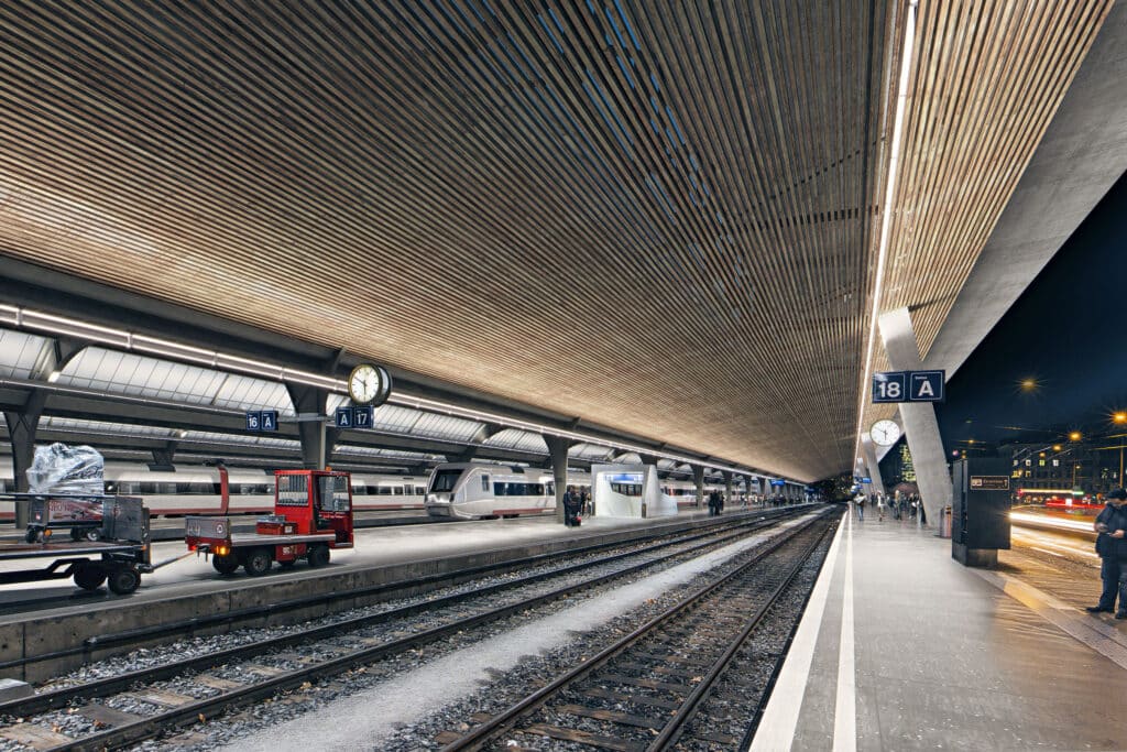 von KGRUPPE Architekten Basel - Ein moderner Bahnhof mit mehreren Gleisen und Bahnsteigen, einer Uhr und Zügen im Hintergrund.