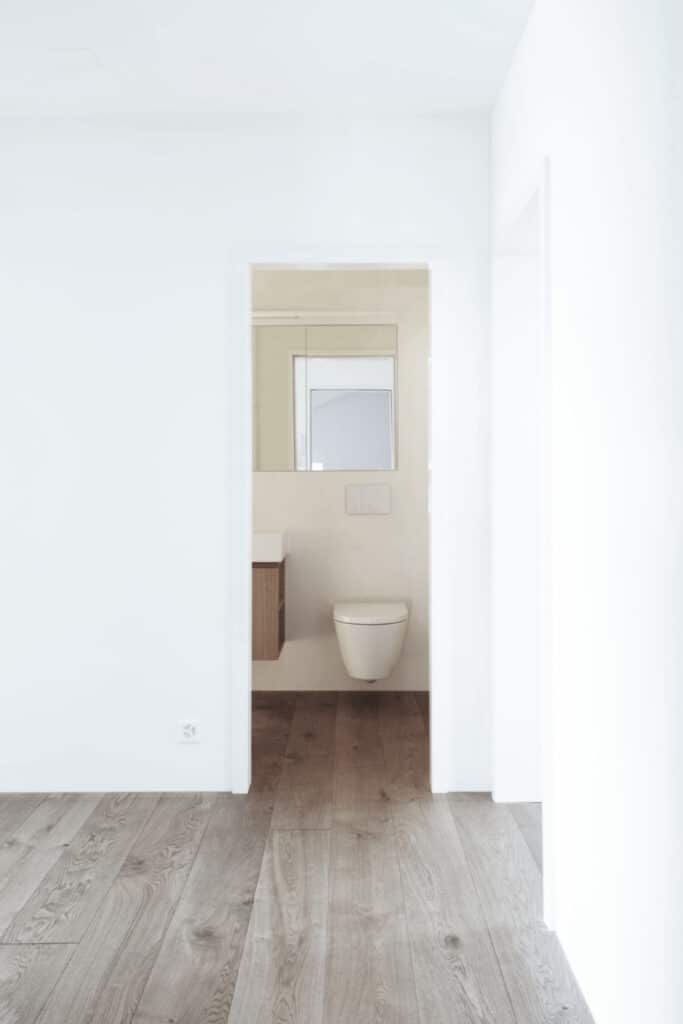 von KGRUPPE Architekten Basel - Minimalistisches Badezimmer mit hängendem WC, Holzboden und weiss gestrichenen Wänden.